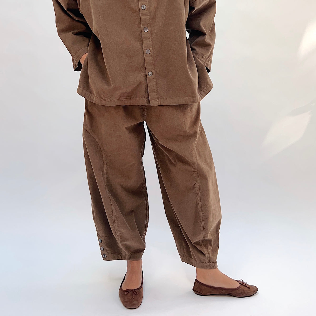 Eleven Stitch Corduroy Doreen Pant in Winter Olive, front view showing the high-rise waist and curved balloon leg with gathered ankle cuffs and three-button closure, styled with a matching corduroy button-front top
