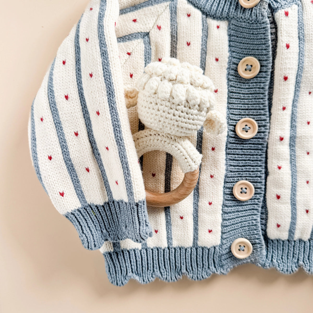 Blue and white striped baby cardigan shwon with wooden teething ring on a beige background