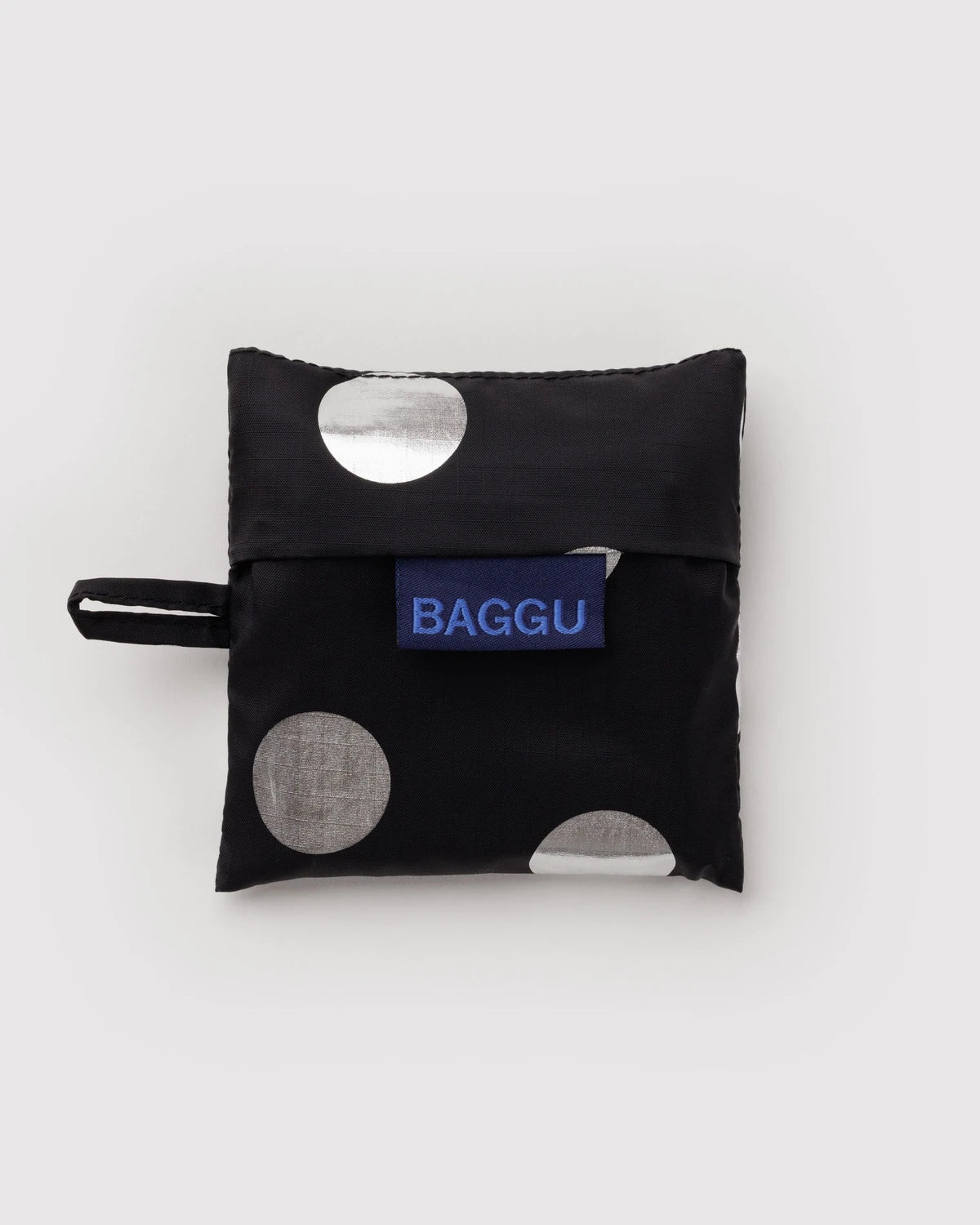 BAGGU Baby Baggu in Metallic Silver Polka Dot, folded into its matching black pouch with silver dots and a visible BAGGU label.
