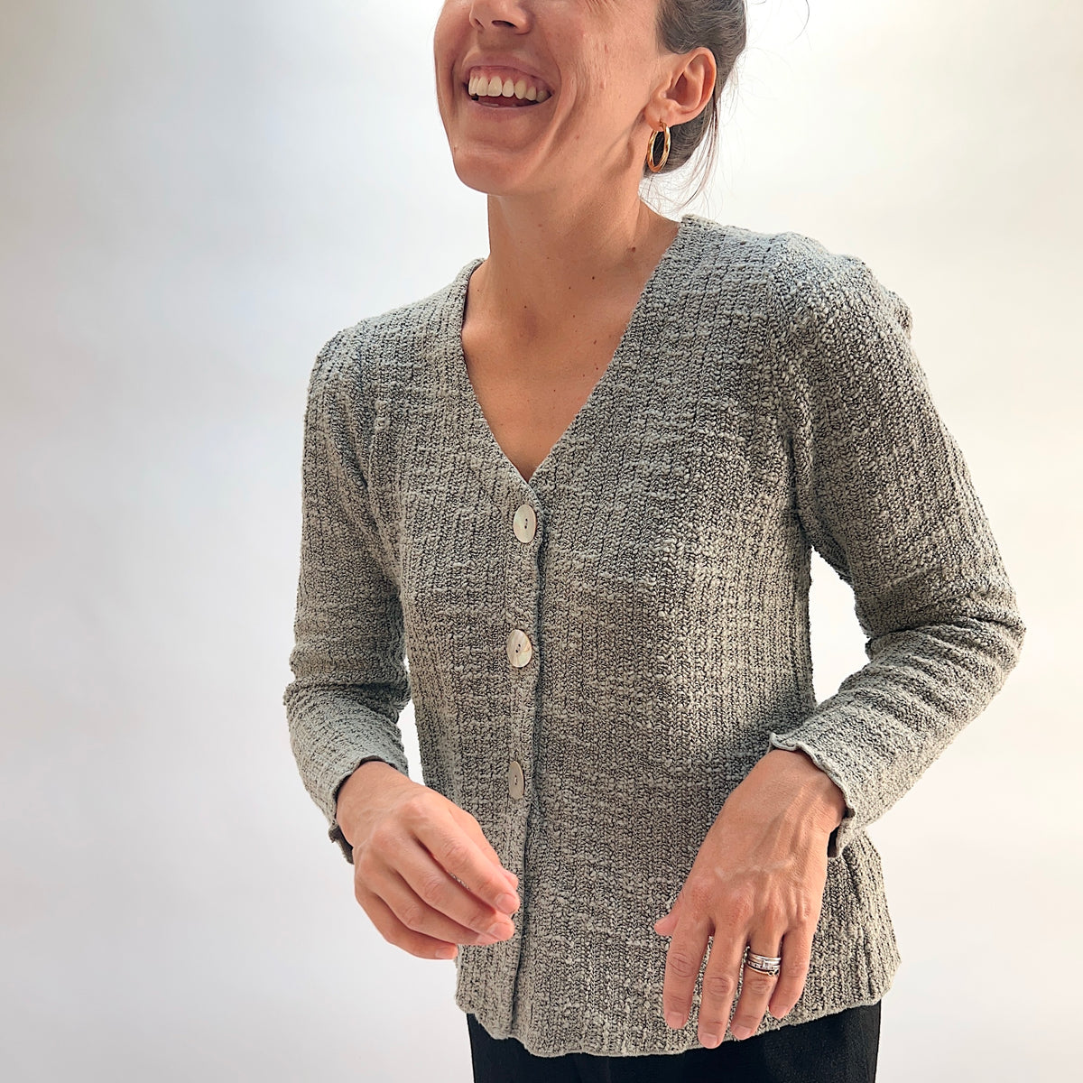 Model wearing the Cut Loose Puff Sleeve Cardigan in Squirrel, close-up front view, warm grey-taupe marled knit cardigan with V-neckline, large natural shell buttons, and scalloped lettuce hem, styled with black pants
