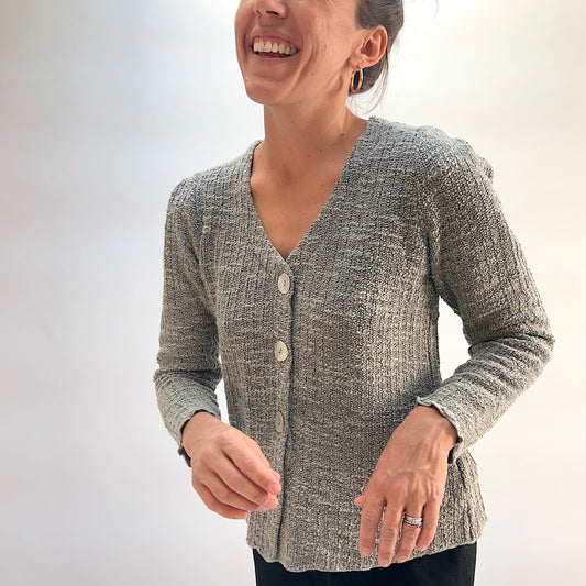 Model wearing the Cut Loose Puff Sleeve Cardigan in Squirrel, close-up front view, warm grey-taupe marled knit cardigan with V-neckline, large natural shell buttons, and scalloped lettuce hem, styled with black pants
