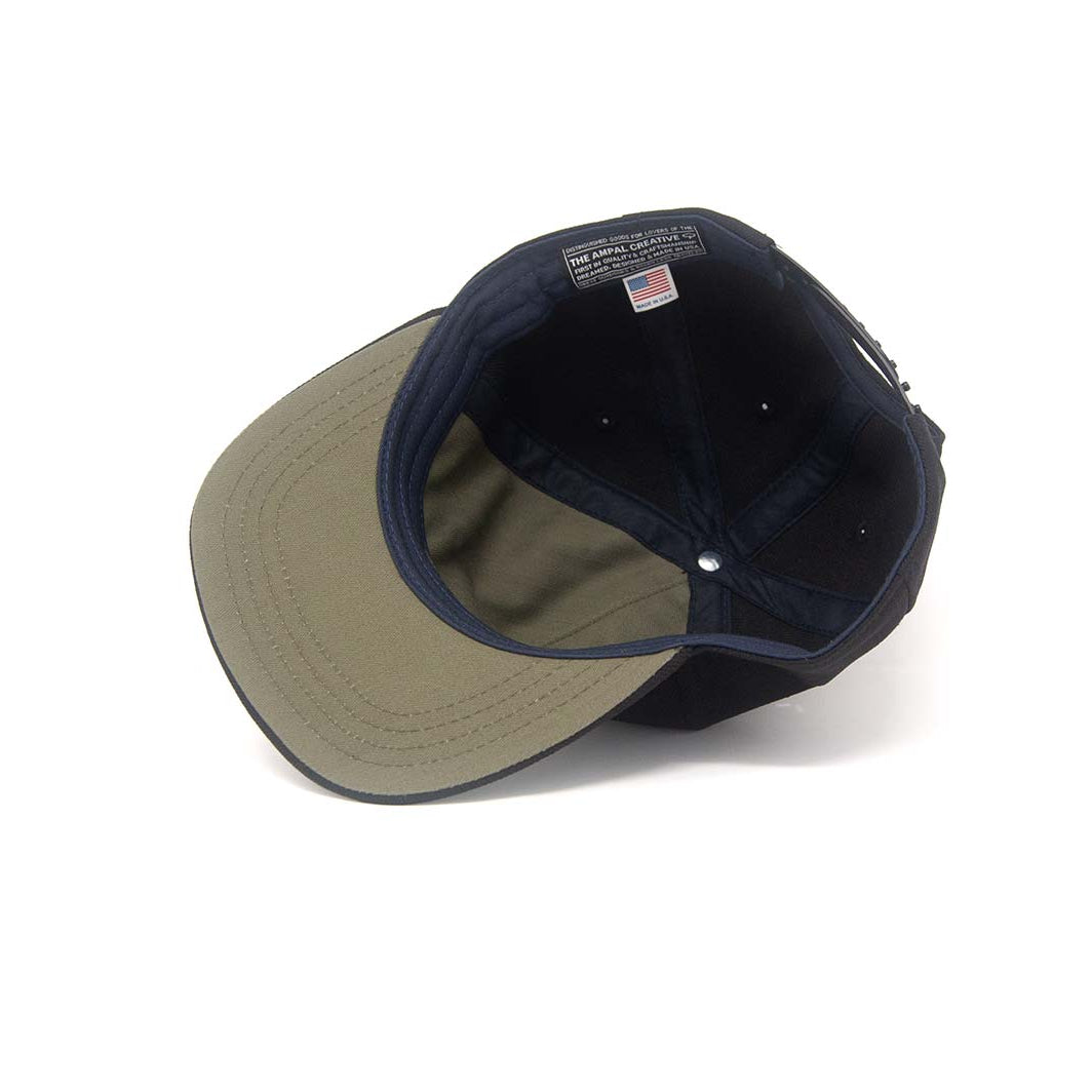 Interior view of the Ampal Creative Skull II Black Snapback, showing the olive underbrim, navy crown lining, The Ampal Creative woven label with USA flag, and snapback closure, on a white background
