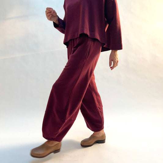 Side view of Bryn Walker Oliver Fleece Pant in Rhone on a model stepping forward, showing the curved legs and tapered hems.
