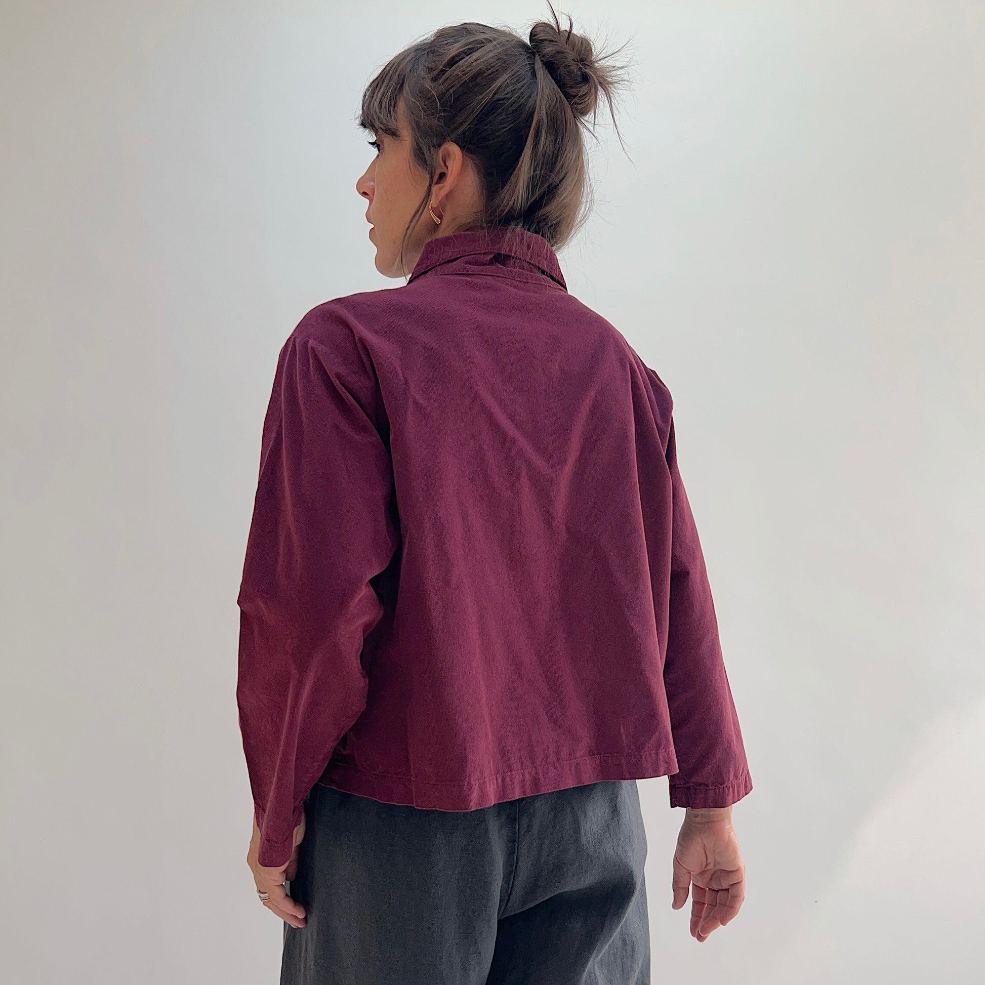 Back view of the Bryn Walker Corduroy Audrey Jacket in Rhone, showing cropped hemline, relaxed silhouette, and burgundy pinwheel corduroy texture, paired with grey trousers
