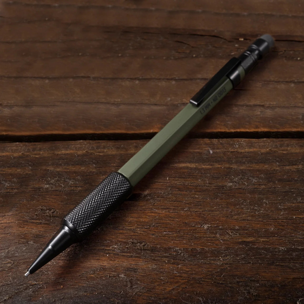 An olive green and black mechanical pencil resting diagonally on a dark brown wooden surface.