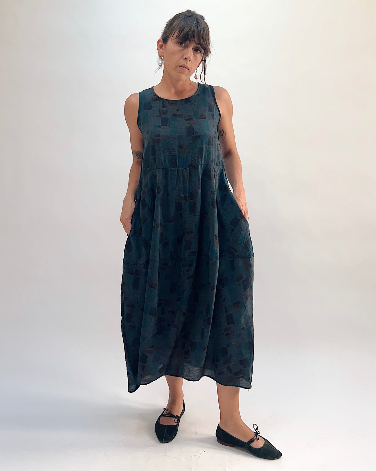 Full front view of the Cut Loose Sea Glass Seamed Parachute Bubble Dress in Etan in deep teal semi-sheer viscose-nylon with abstract block print, hands in patch side pockets
