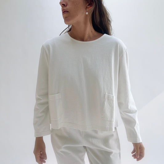 Model wearing a cream boxy cotton top with two front patch pockets and 3/4 sleeves, hands on hips against a white background.
