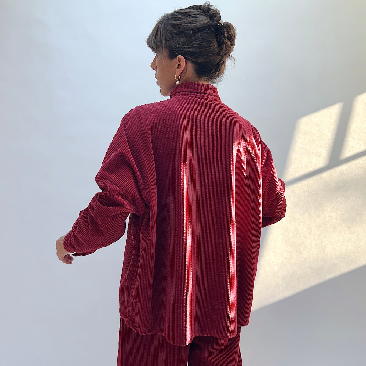 Back view of the Lux Corduroy Oversized Shirt in Maraschino on a model, showing the vertical corduroy texture and curved hem.
