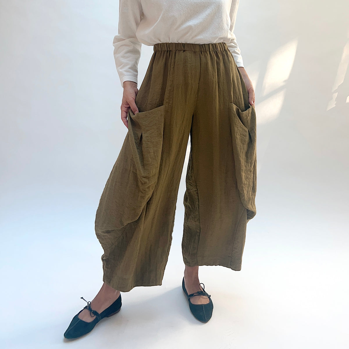 Eleven Stitch Double Pocket Crinkle Travel Pant in Olive, front view with model holding the large side pockets open.
