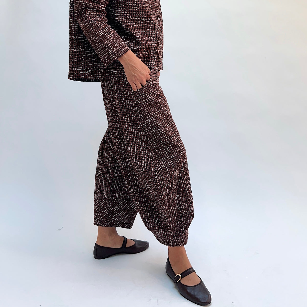 Niche Izzie Pant in Cocoa Check, side view showing the relaxed hip and tapered ankle in dark brown textured check print with front pocket detail
