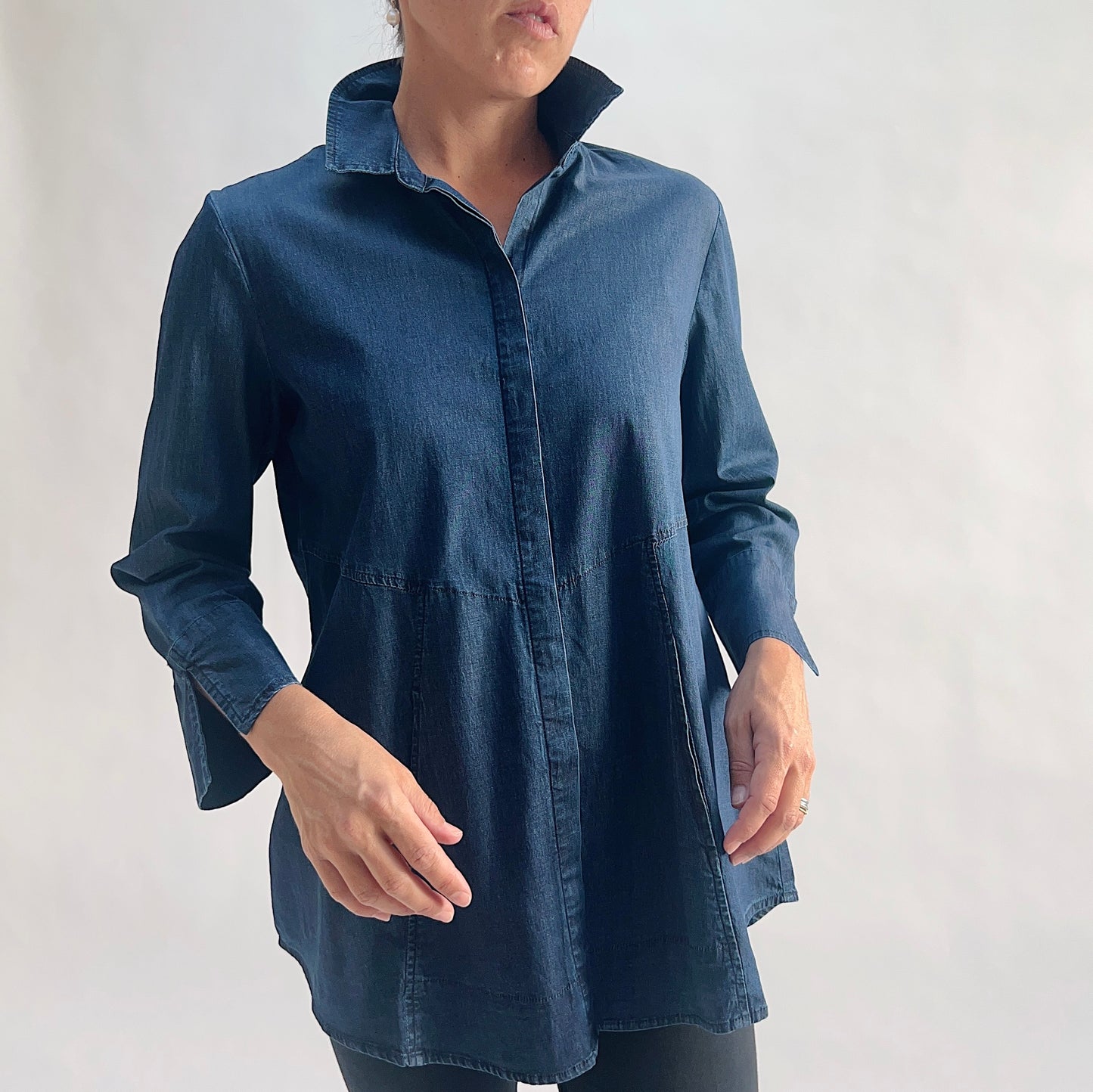 Close front view of model wearing a lightweight dark indigo denim tunic shirt with hidden front placket, point collar, and 3/4 sleeves with slit cuffs, arms at sides, showing the empire seam and
