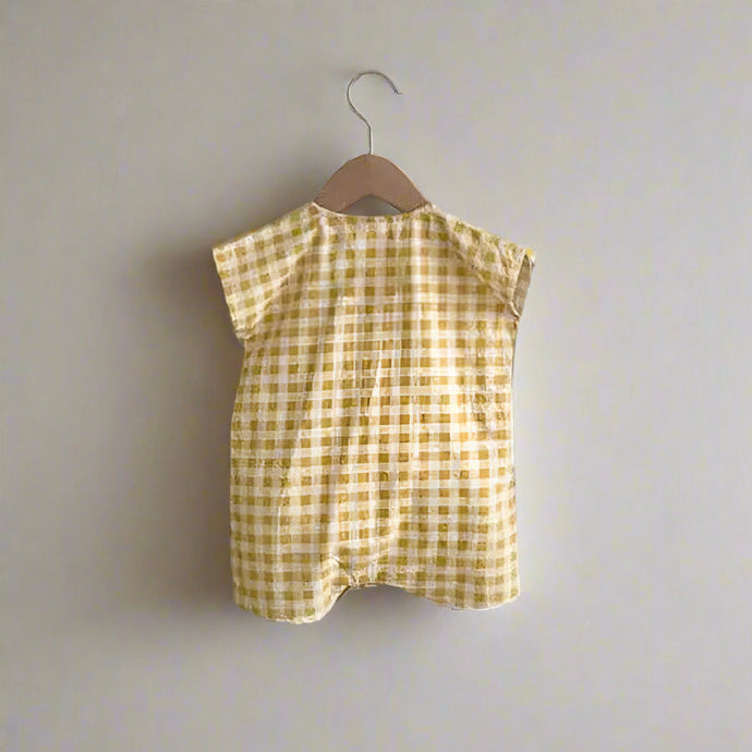 Yellow checkered baby romper on a hanger against a white wall.