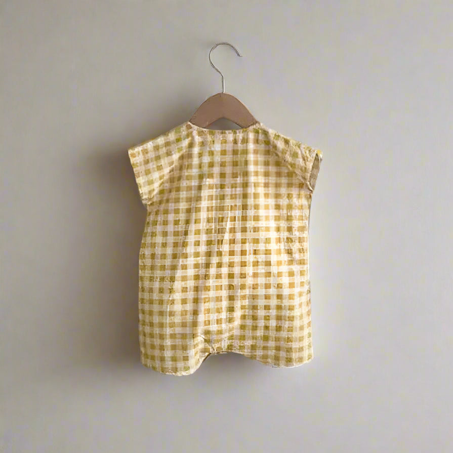 Yellow checkered baby romper on a hanger against a white wall.