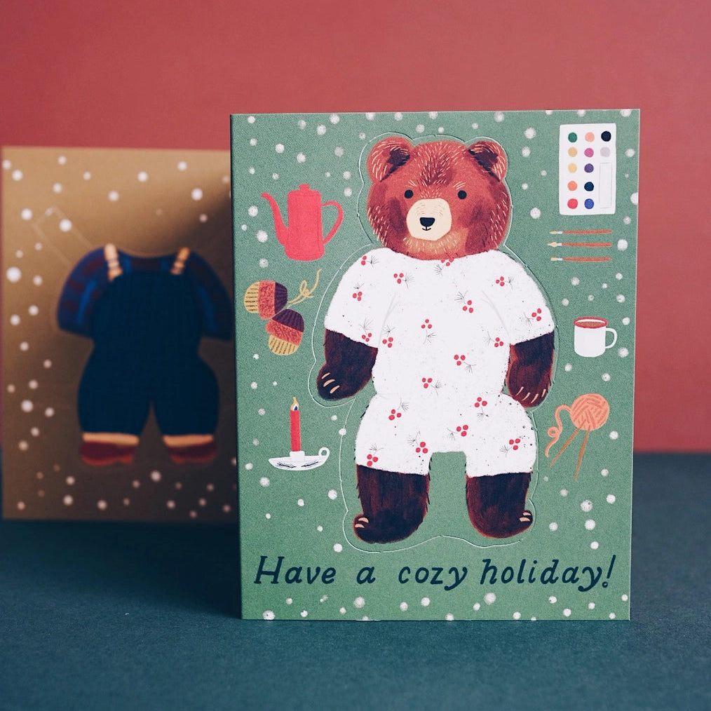 Small Adventure Bear Paper Doll Cozy Holiday Card, front showing a bear in floral pajamas and the words “Have a cozy holiday!”
background.