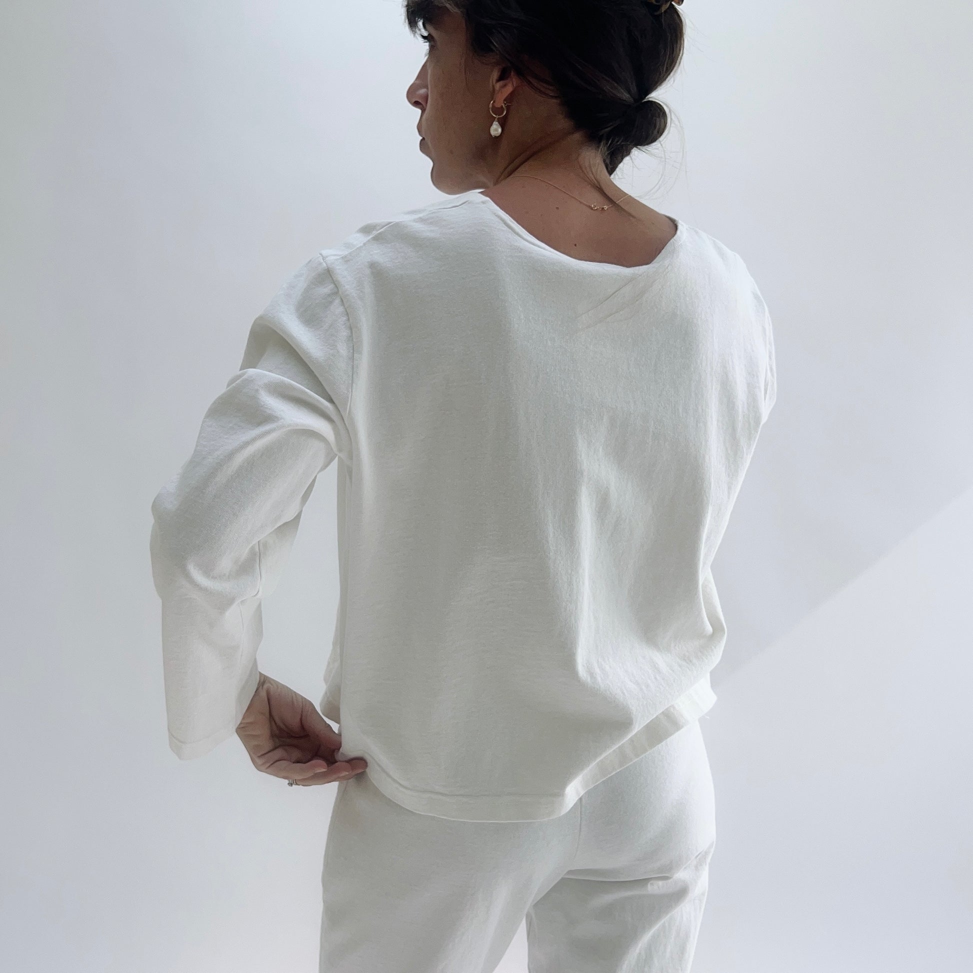 Front view of model in a cream boxy 3/4 sleeve cotton top with two patch pockets, styled with cream wide-leg pants against a white background.
