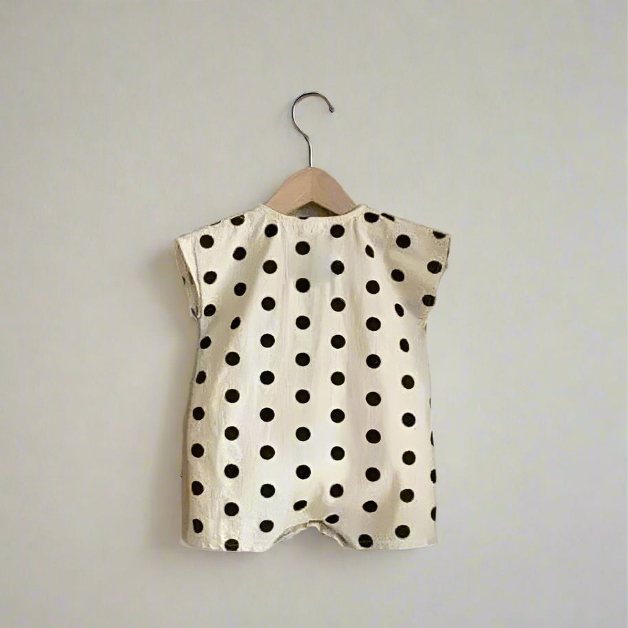 Polka dot baby romper on a hanger against a textured wall.
