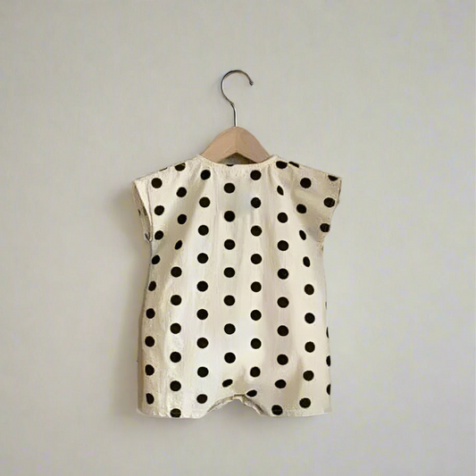 Polka dot baby romper on a hanger against a textured wall.