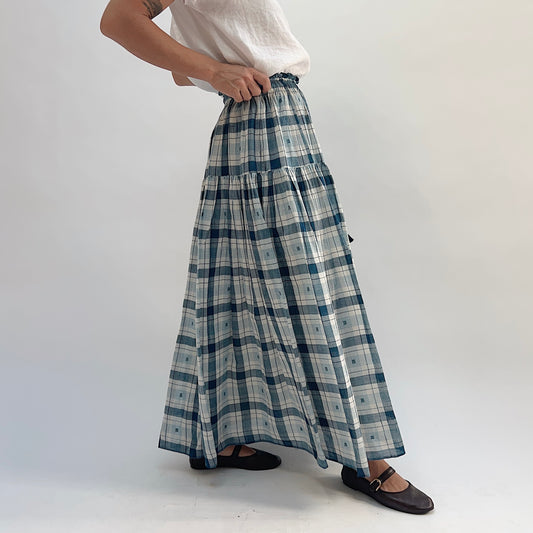 DVAA Denise Skirt in Blue Plaid, tiered maxi skirt with ruffled elastic waist and tassel tie detail, styled with a white tee — side view showing full length and drape
