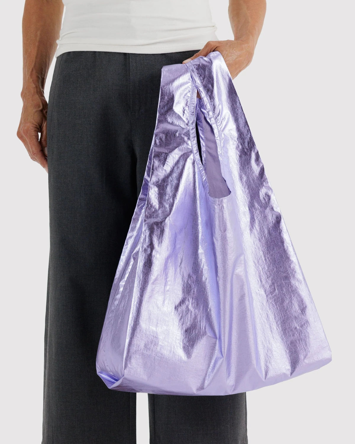 BAGGU Standard Baggu in Metallic Lavender, held by a model at their side to show the bag’s size and reflective finish.
