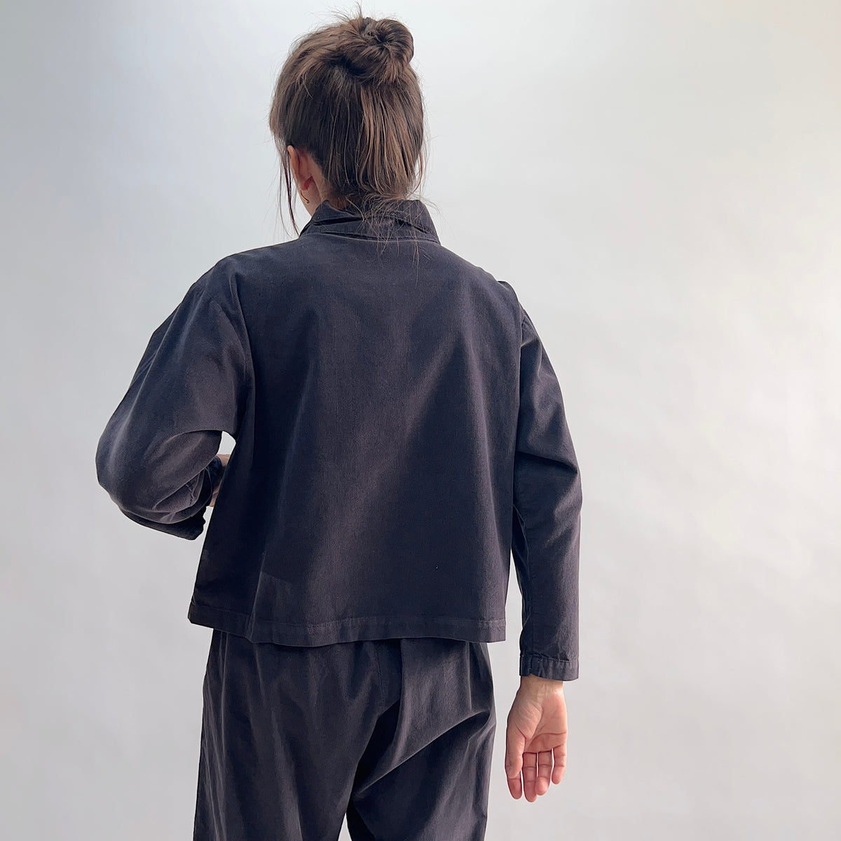 Back view of the Bryn Walker Corduroy Audrey Jacket in Fig, showing cropped hemline, relaxed silhouette, and charcoal pinwheel corduroy texture, paired with matching trousers

