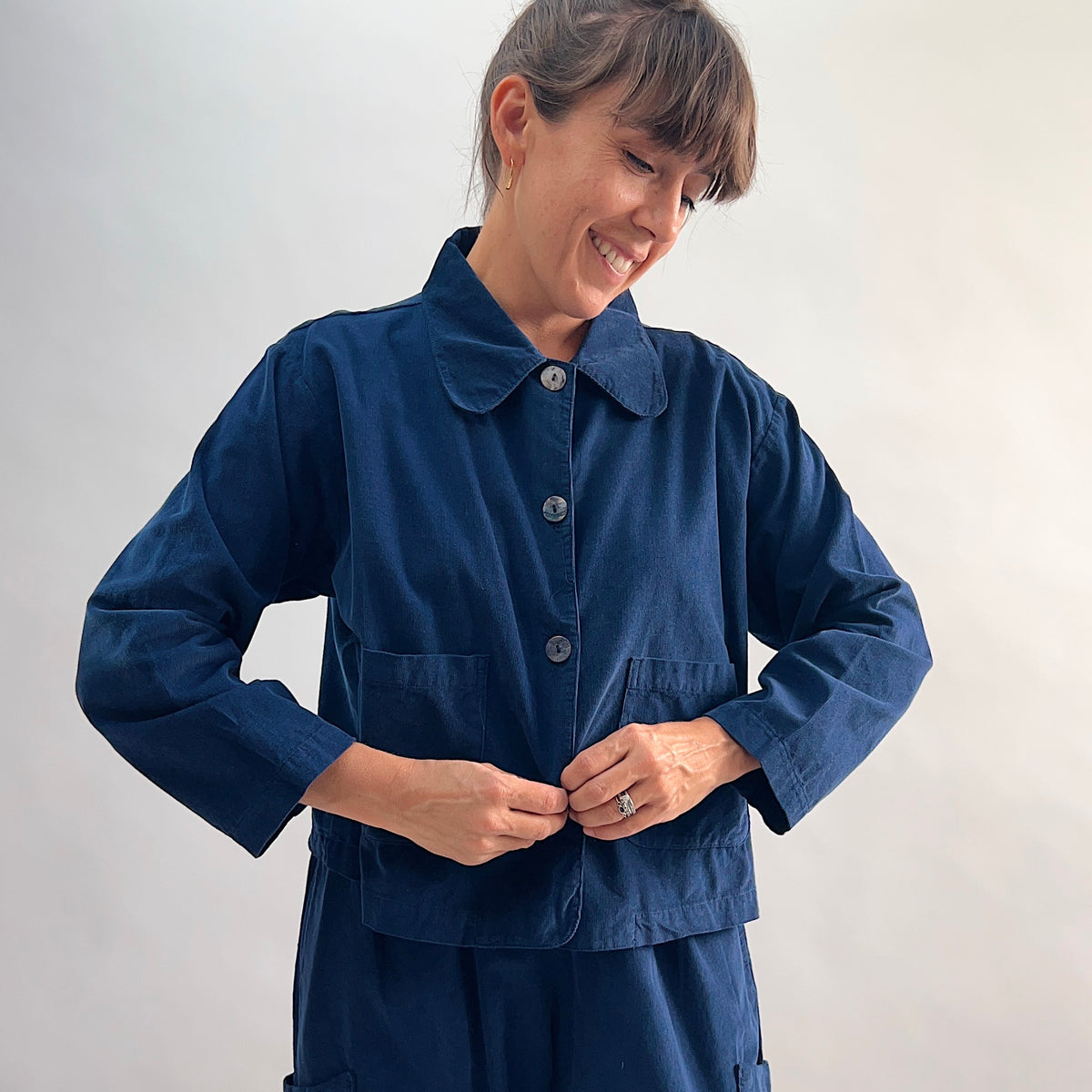 Model smiling and buttoning the Bryn Walker Corduroy Audrey Jacket in Nova, front view highlighting shell buttons, patch pockets, and pinwheel corduroy texture
