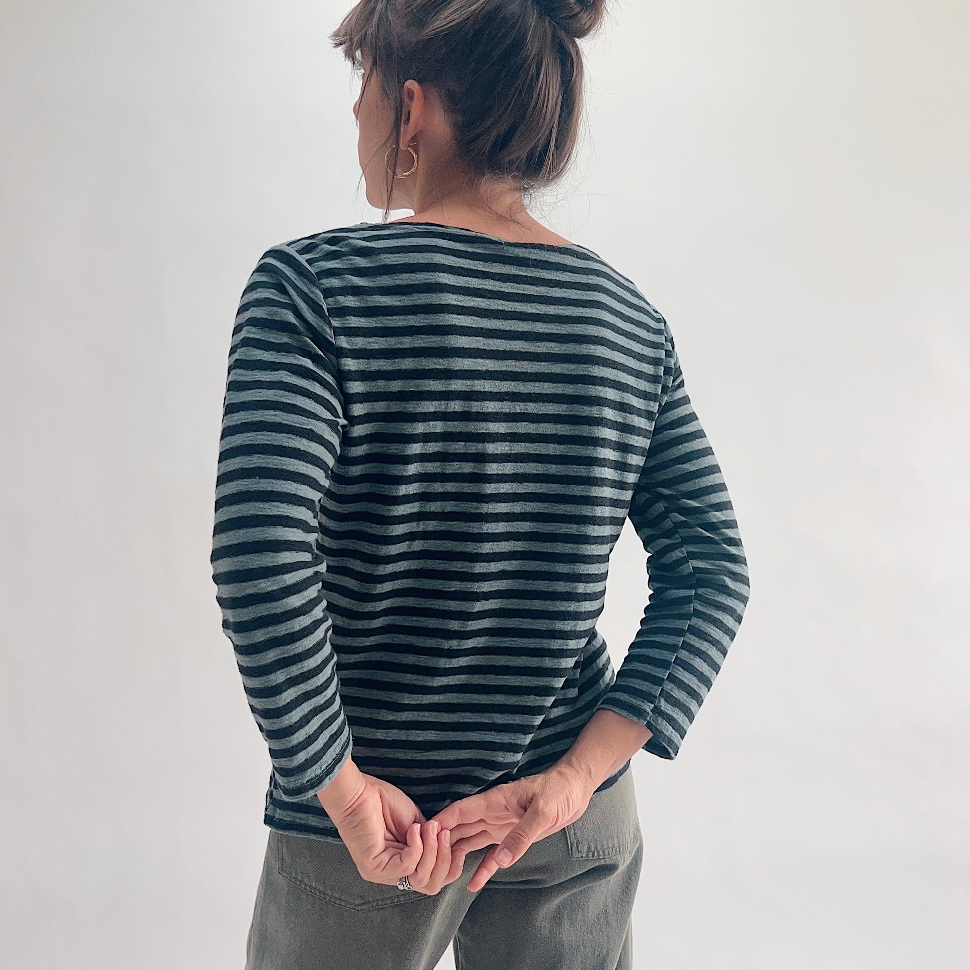 Back view of model wearing an iron stripe 3/4 sleeve boatneck tee, hands clasped behind her back, showing the clean back seam and 3/4 sleeve length.
