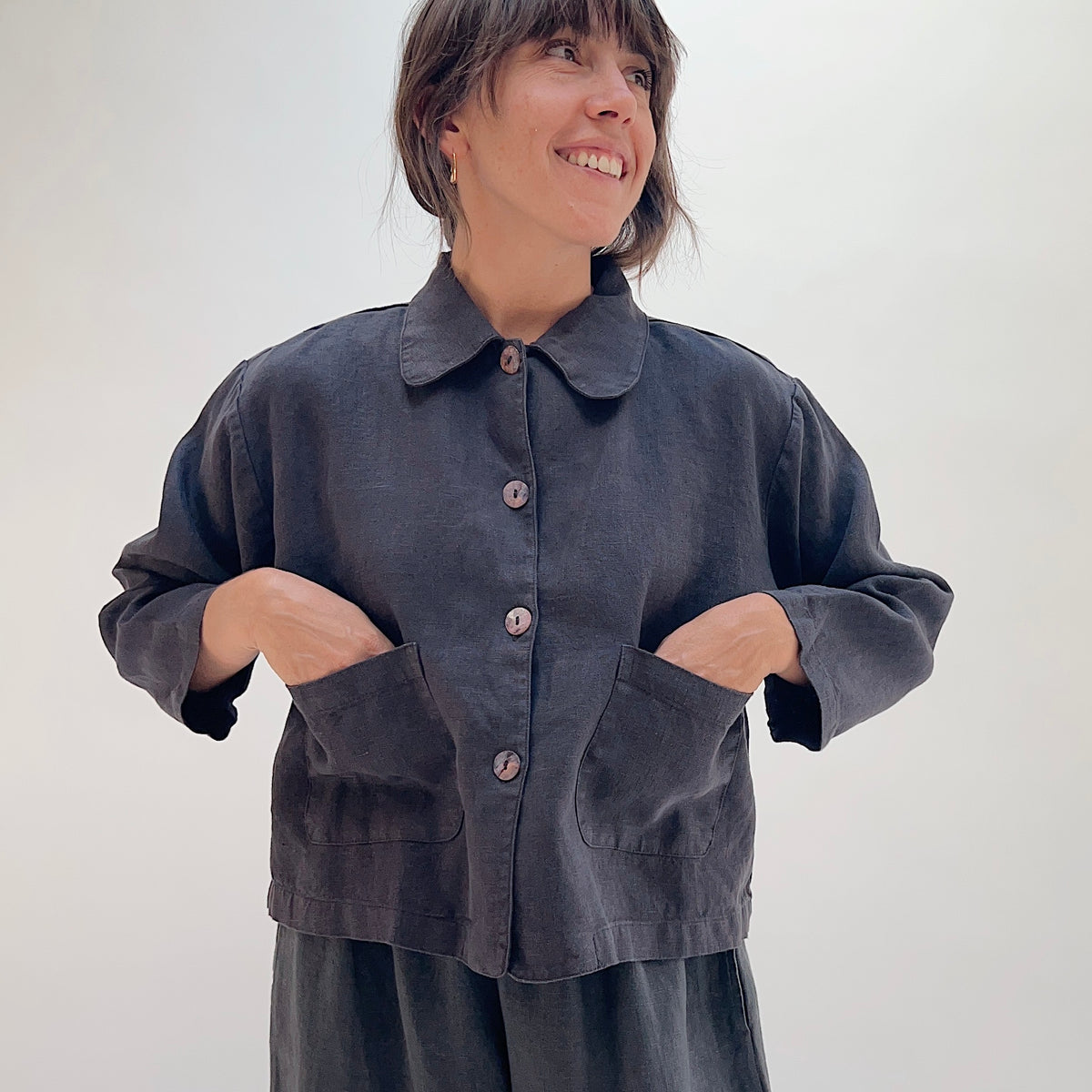 Model smiling and wearing the Bryn Walker Heavy Linen Audrey Jacket in Fig with hands in patch pockets, front view
