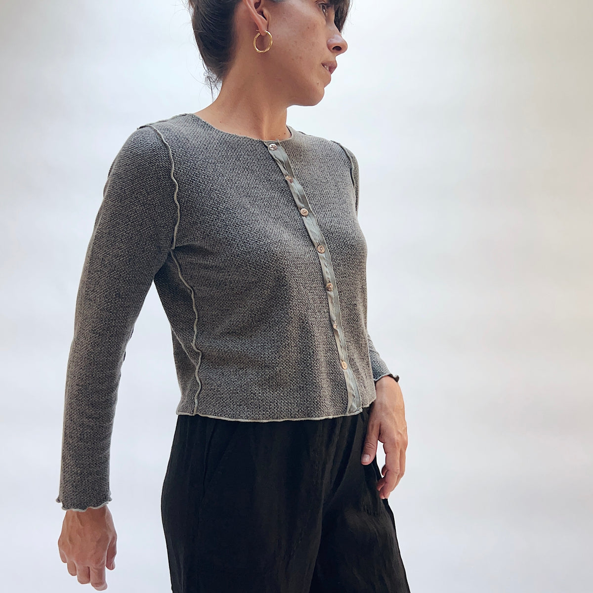 Model wearing the Marled Knit Cropped Cardigan in Squirrel, three-quarter side view, fitted cropped button-front cardigan in heathered gray marled knit with scalloped edges, styled with black trousers
