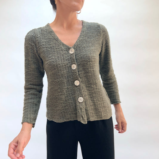 Model wearing the Cut Loose Puff Sleeve Cardigan in Kelp, three-quarter front view, olive green marled knit cardigan with V-neckline, four large natural shell buttons, gently puffed shoulders, and scalloped lettuce hem, styled with black pants
