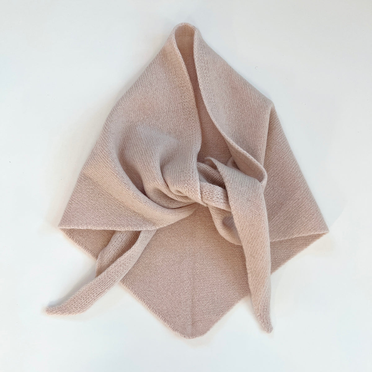 Flat lay view of the Cream merino wool triangle scarf arranged with a loose knot and pointed ends.
