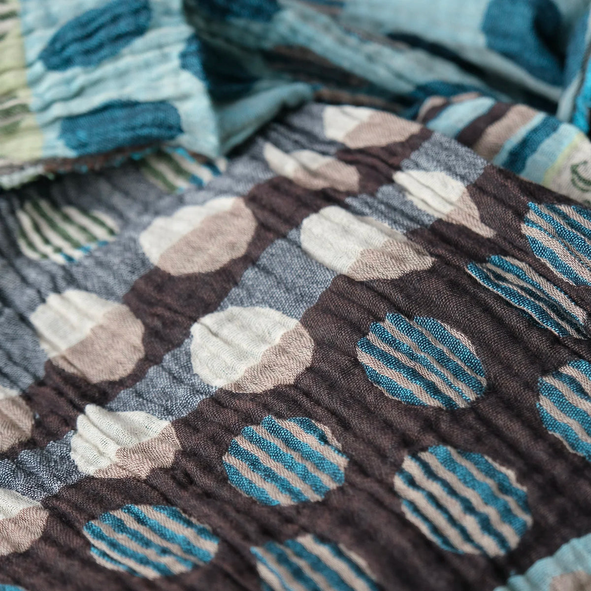 Close-up detail of the Létol Coline Scarf in Marron Turquoise, showing the Jacquard-woven texture of the reverse side — large cream and taupe polka dots on a deep brown ground with rows of teal striped dots, alongside the folded obverse showing light blue horizontal stripes and the teal striped border edge, highlighting the richly textured weave and reversible construction
