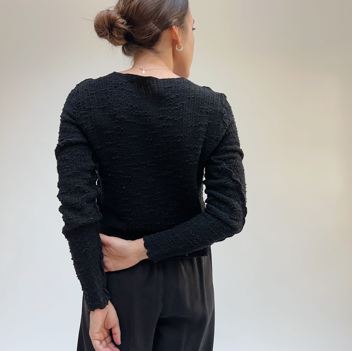 Back view on a model of a black textured knit crop cardigan.
