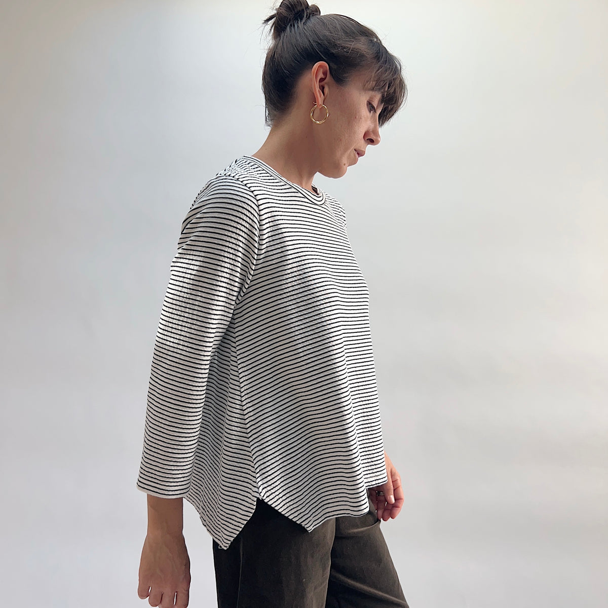Cut Loose Striped Side Vent Crew in Laundered, white and black fine-stripe crewneck top with boxy silhouette and side vent, model looking down, paired with dark wide-leg trousers — side view showing drape and length
