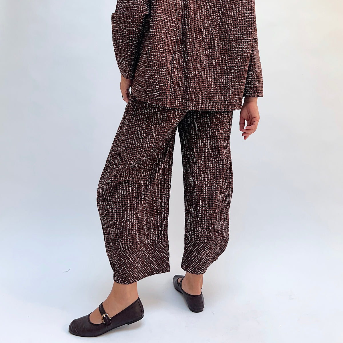 Niche Izzie Pant in Cocoa Check, three-quarter view showing the wide-leg tapered silhouette in dark brown textured check print
