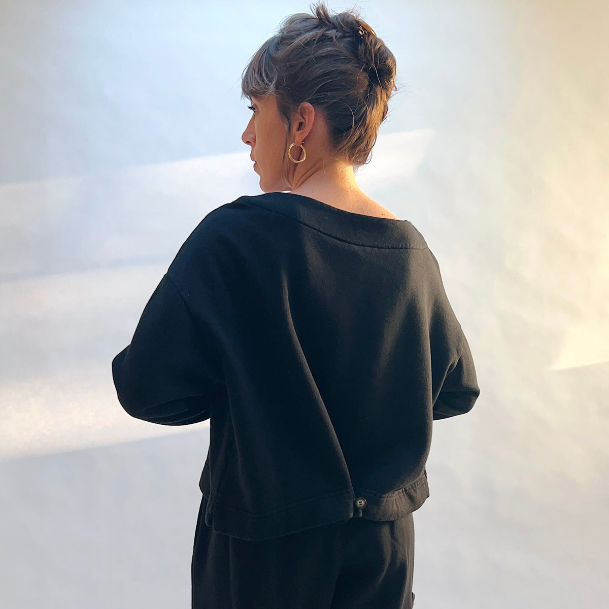 Back view of Button Back Fleece Pullover in Black with the hem buttoned to create a gathered shape.
