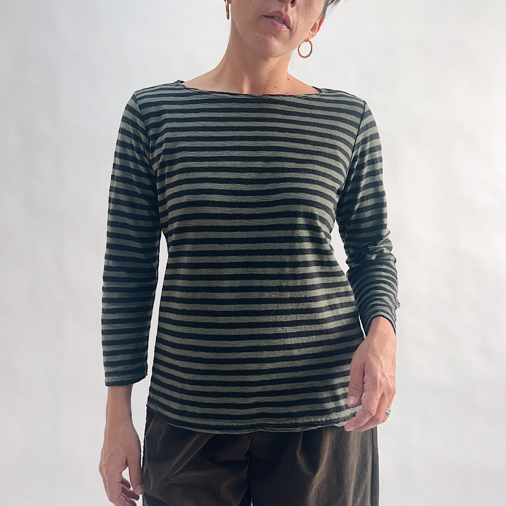 Front view of model wearing a kelp green and black horizontal stripe boatneck tee with 3/4 sleeves, arms at sides, showing the wide boatneck neckline and relaxed fit, styled with dark charcoal wide-leg pants against a white background.
