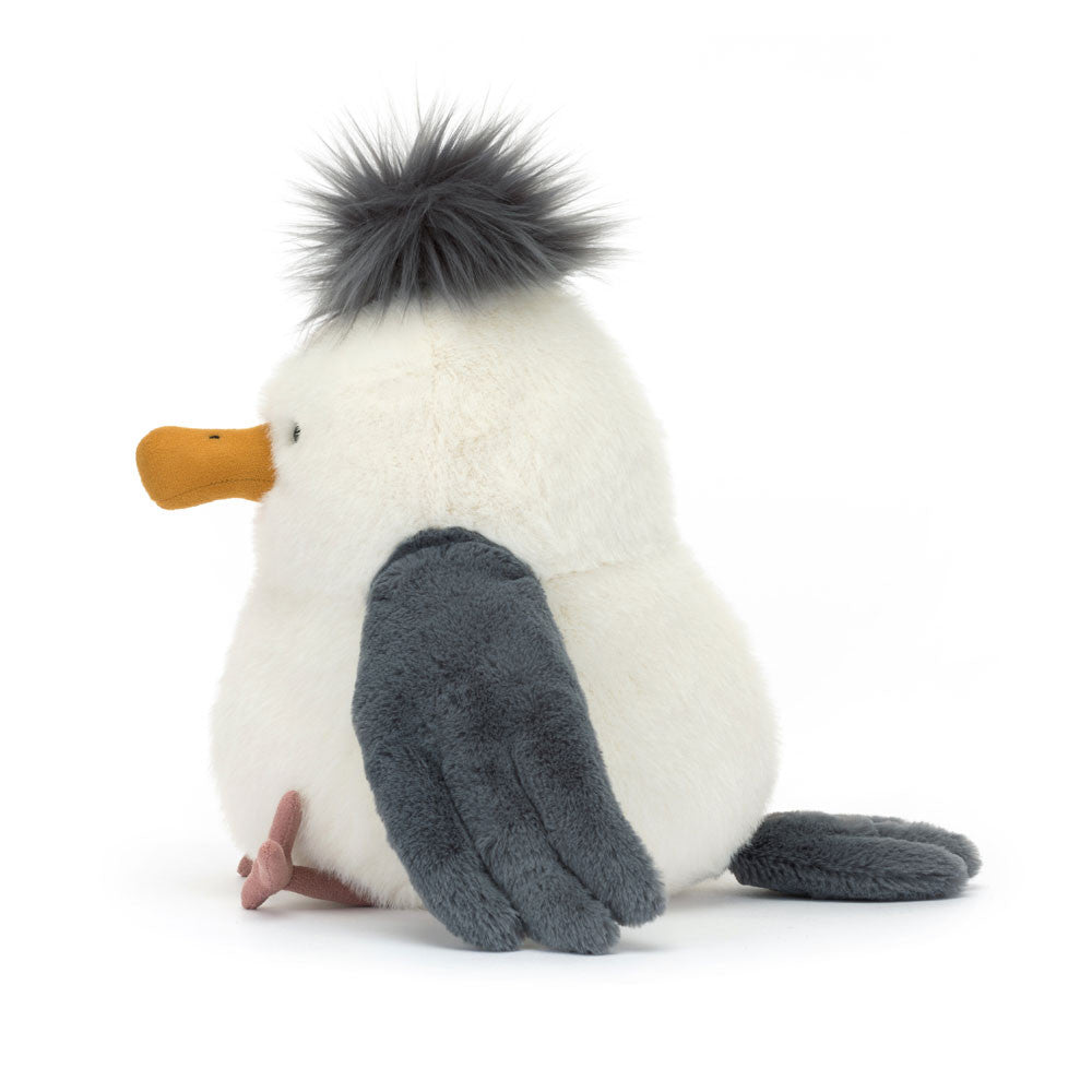 Side profile of Jellycat Chip Seagull showing the round white body, grey pom-pom crest, yellow beak in profile, one grey wing, and a pink webbed foot, on a white background