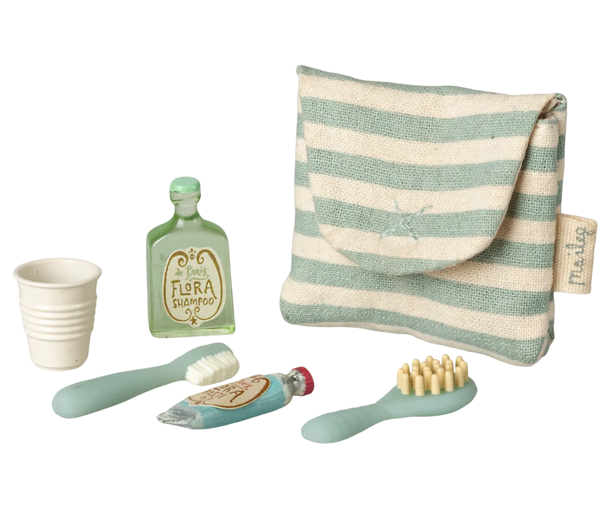 Maileg Toothbrush Set in Blue Striped Bag — angled view of the blue striped Maileg toiletry bag alongside miniature accessories including a Flora Shampoo bottle, ribbed cup, toothbrush, toothpaste tube, and hairbrush
