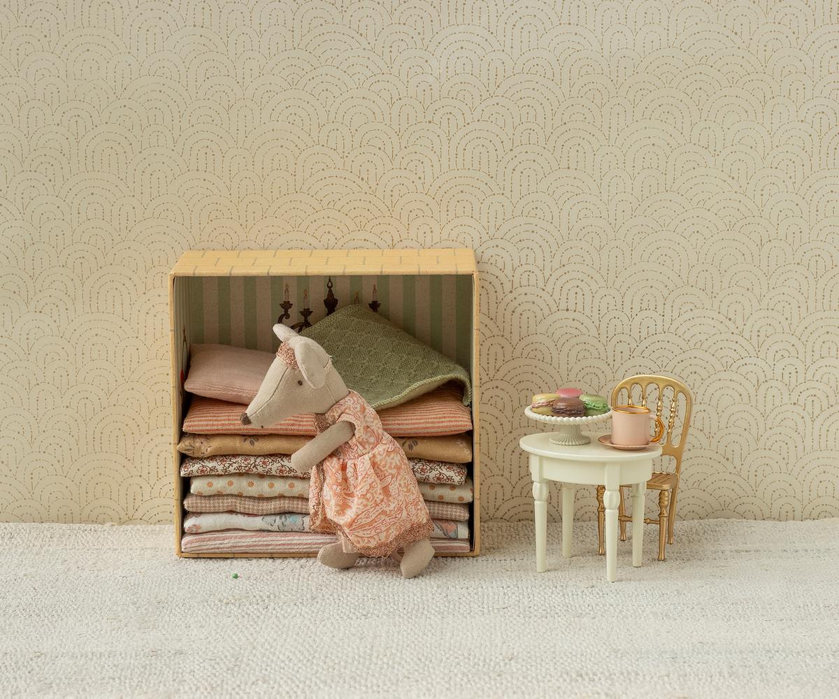 Maileg Princess and the Pea Big Sister Mouse — lifestyle scene of princess mouse doll in a pink lace dress resting on a stack of folded fabric mattresses inside the castle box, styled beside a miniature table with macarons and a gold chair
