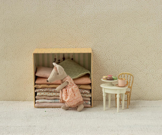Maileg Princess and the Pea Big Sister Mouse — lifestyle scene of princess mouse doll in a pink lace dress resting on a stack of folded fabric mattresses inside the castle box, styled beside a miniature table with macarons and a gold chair
