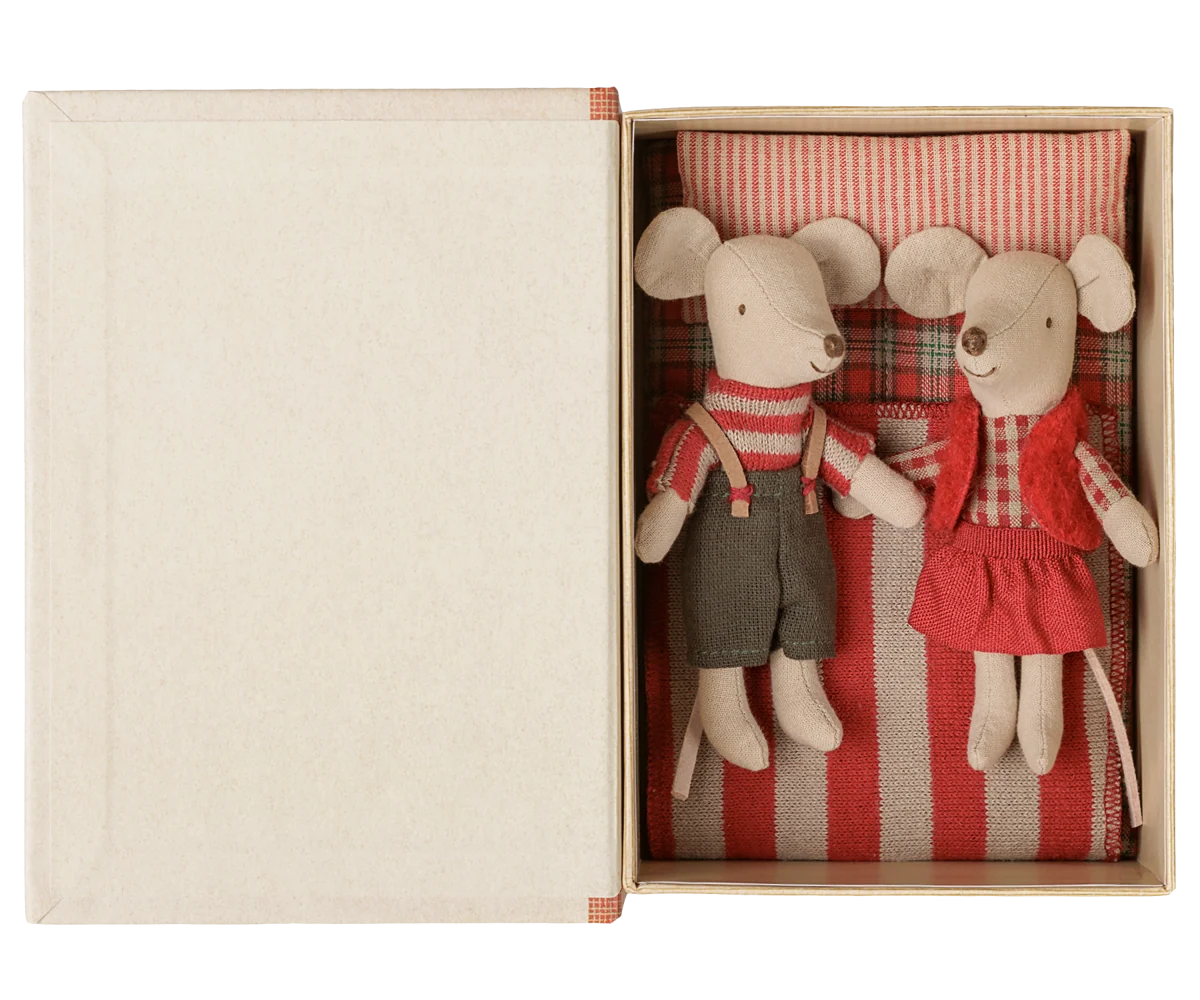 Maileg Little Brother and Little Sister Christmas mice tucked side by side into an open book box with red striped bedding and a plaid pillow.

