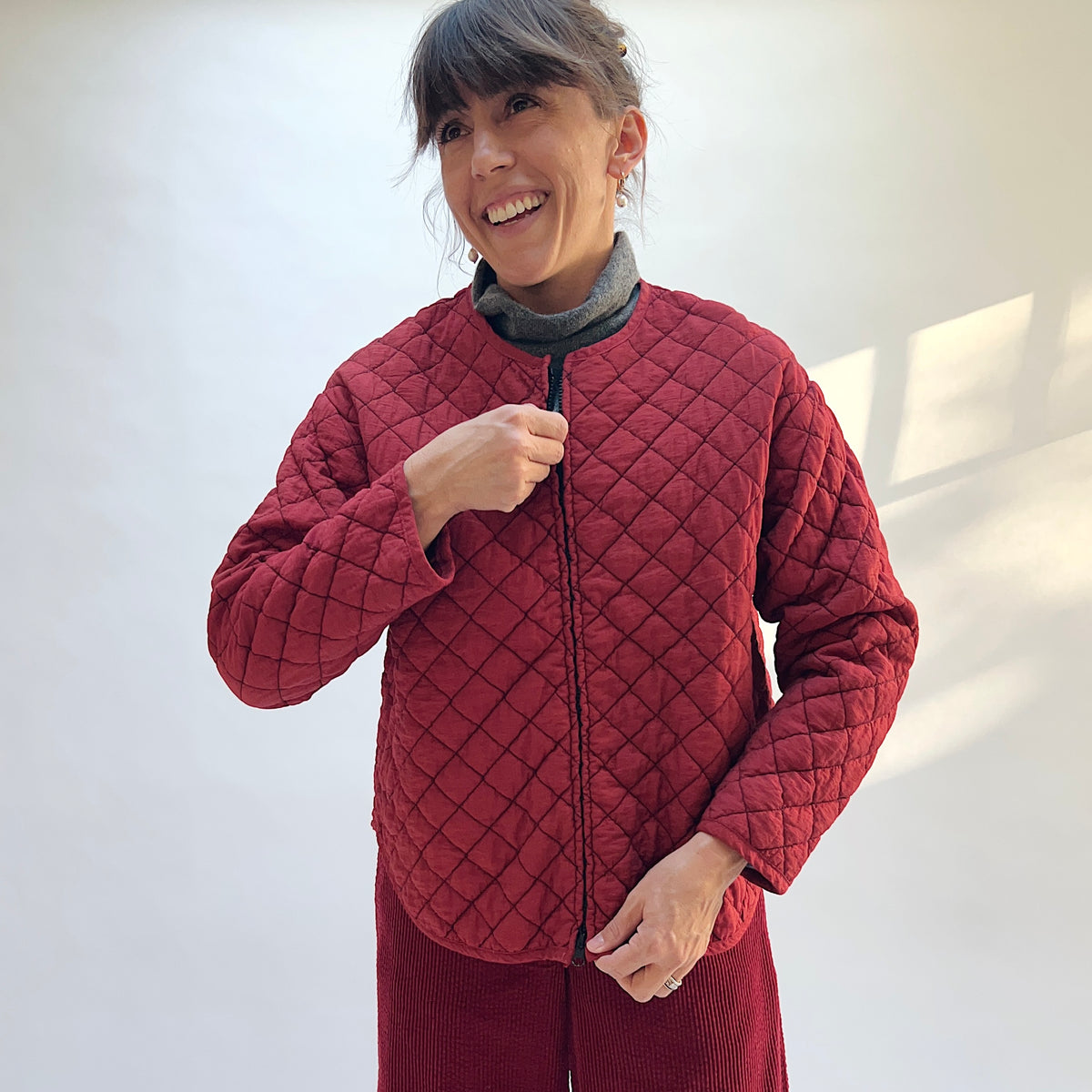 Model wearing the Cut Loose Quilted Bomber Jacket in Maraschino, holding the front zipper and showing the diamond quilting.
