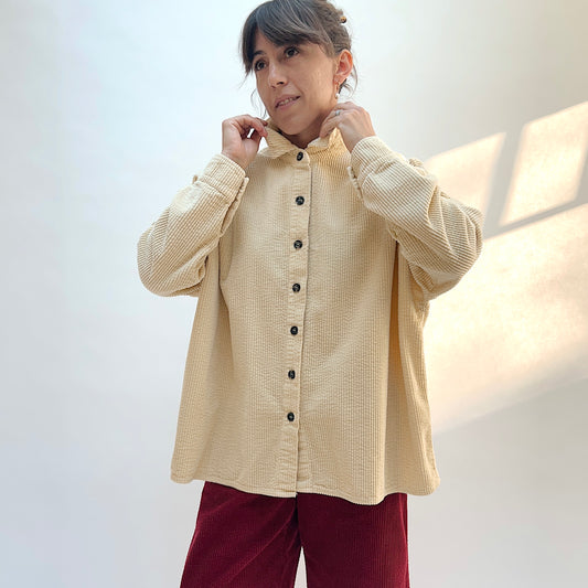 Model adjusting the collar of the Cut Loose Lux Corduroy Oversized Shirt in Glow, showing the pale cream fabric and dark front buttons.
