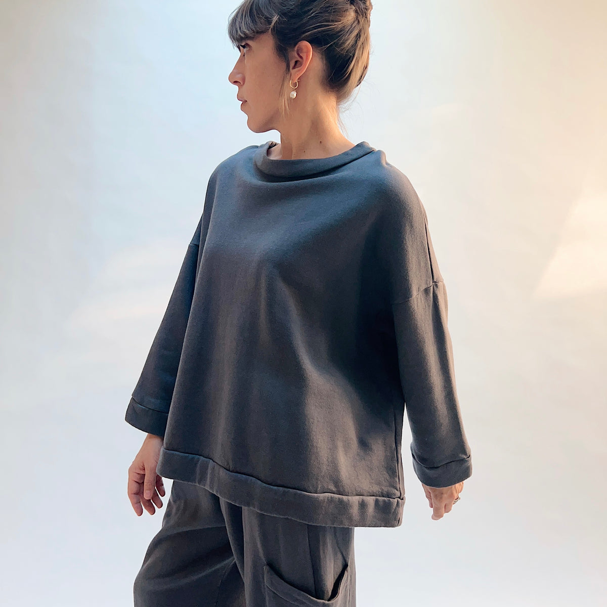Angled front view of Bryn Walker Alden Fleece Sweatshirt in Moonlight on a model, showing the draped neckline, dropped shoulders, and banded hem.
