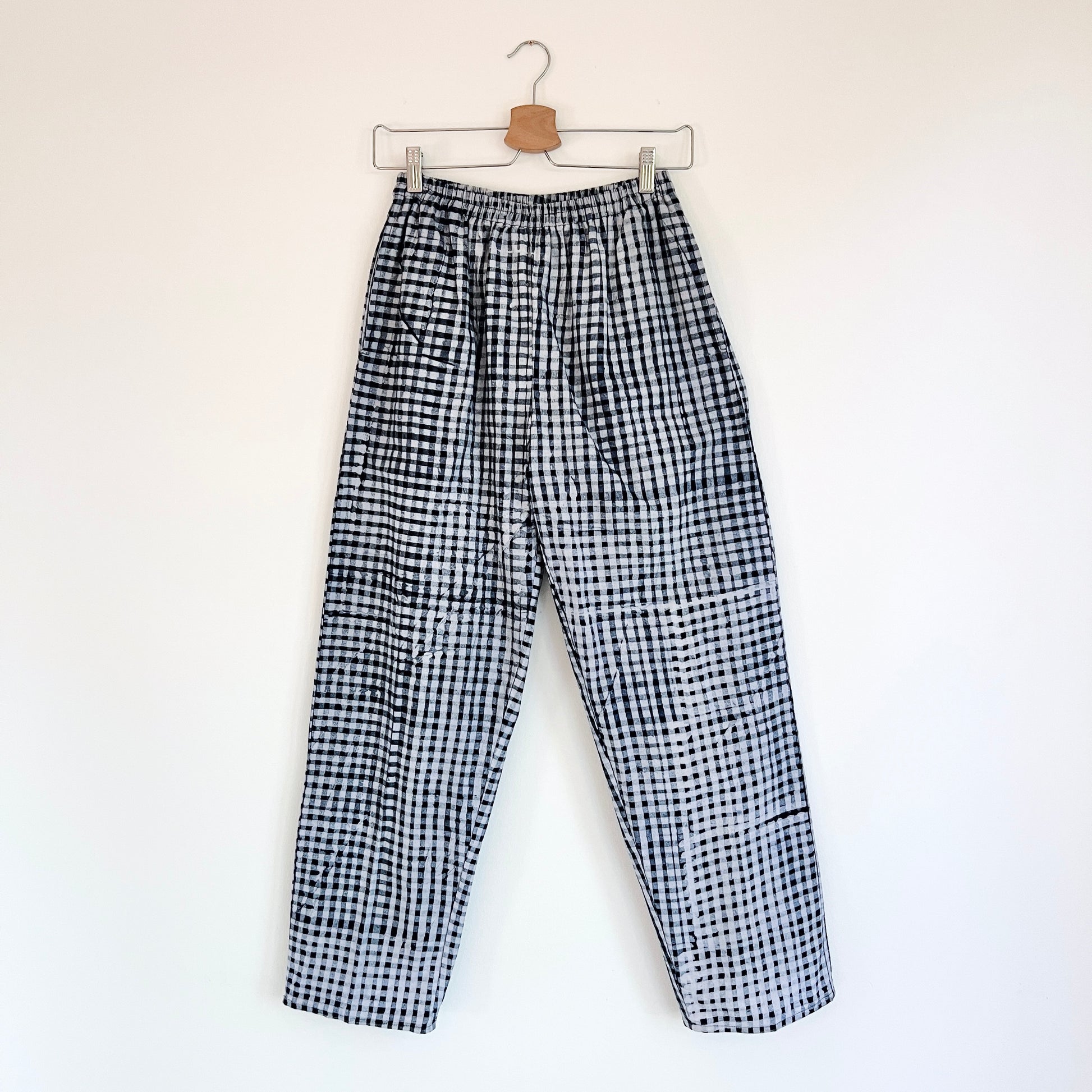 Lazy Pants in Indigo Dots — full-length front view on hanger, loose-fit unisex pants in hand-dyed indigo and white batik check print with elastic waist
