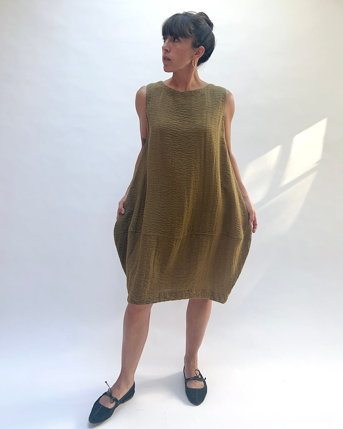 Eleven Stitch Travel Bubble Dress in Teak, front view with model holding the sides to show the bubble shape.
