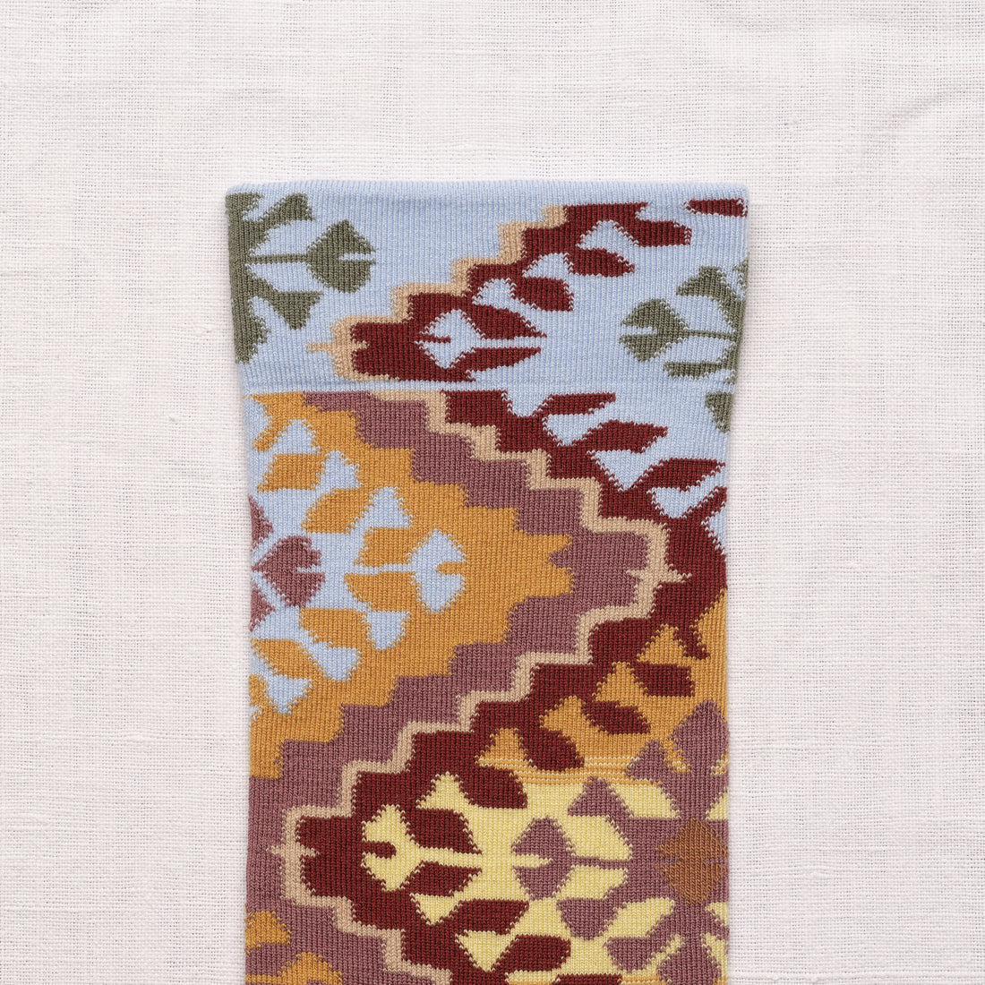 Bonne Maison Le Tapis Multicolor Socks, close-up of the cuff showing the kilim-inspired geometric pattern in sky blue, burgundy, and ochre