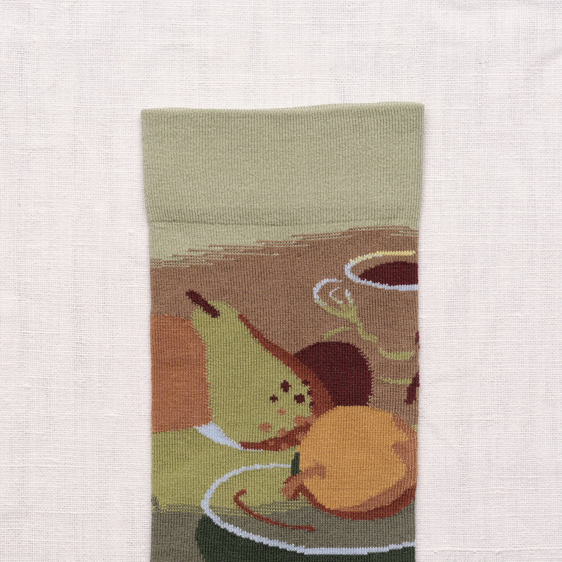 Bonne Maison Le Brunch Socks, close-up of the cuff showing the illustrated brunch scene with a pear, orange, coffee cup, and sage cuff detail

