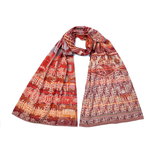 Létol Diego Scarf in Paprika, draped and loosely knotted against a white background, showing a reversible Jacquard-woven organic cotton scarf in maroon, red pepper, terracotta, sand, and orange with blue and turquoise accents — one side featuring stylized fish, botanical, and animal motifs on horizontal bands, the other showing bold abstract letterform and geometric patterns — with a woven Létol label visible at the lower left
