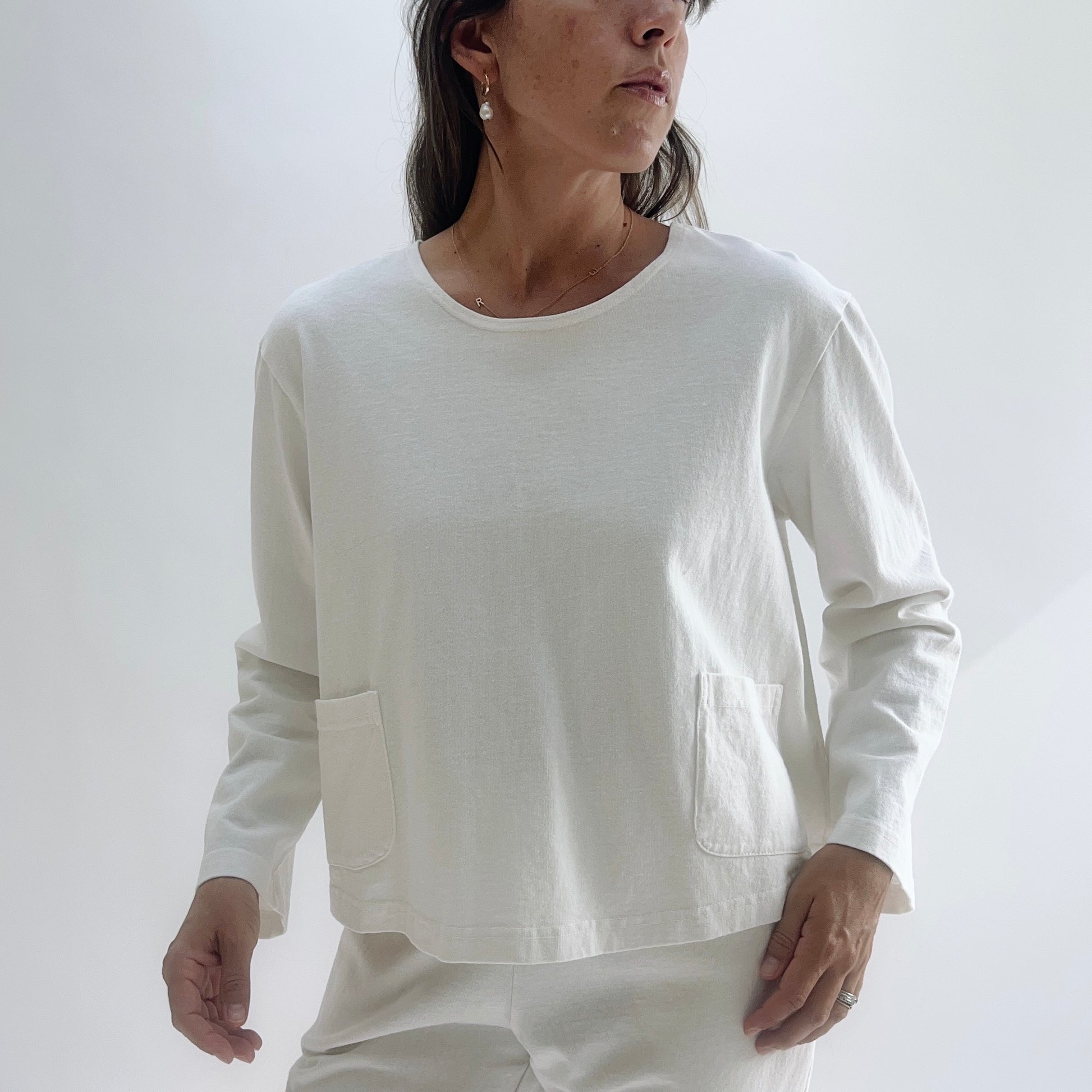 Close-up front view of a cream boxy 3/4 sleeve cotton top with two lower patch pockets, worn with cream wide-leg trousers.
